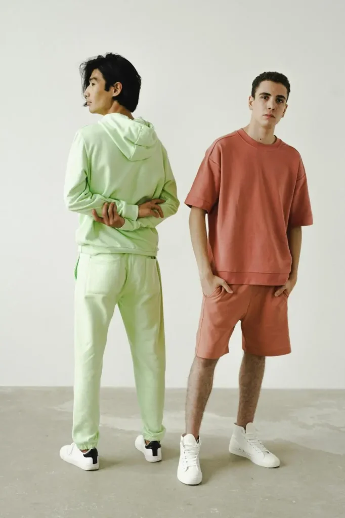 Two young men in vibrant pink and green clothing pose side by side, showcasing their colorful styles.
