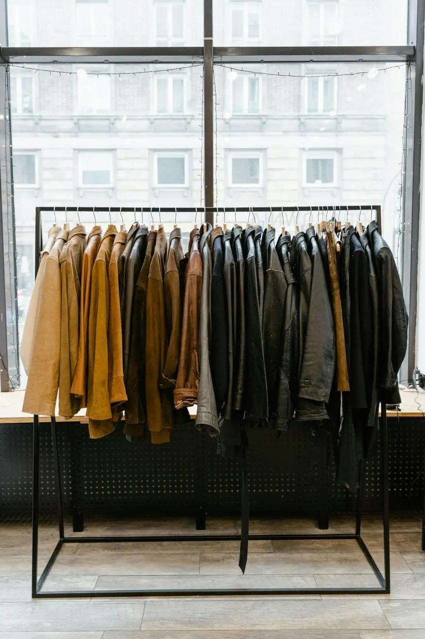 A collection of jackets and coats hanging on a rack, situated in front of a window that lets in sunlight.